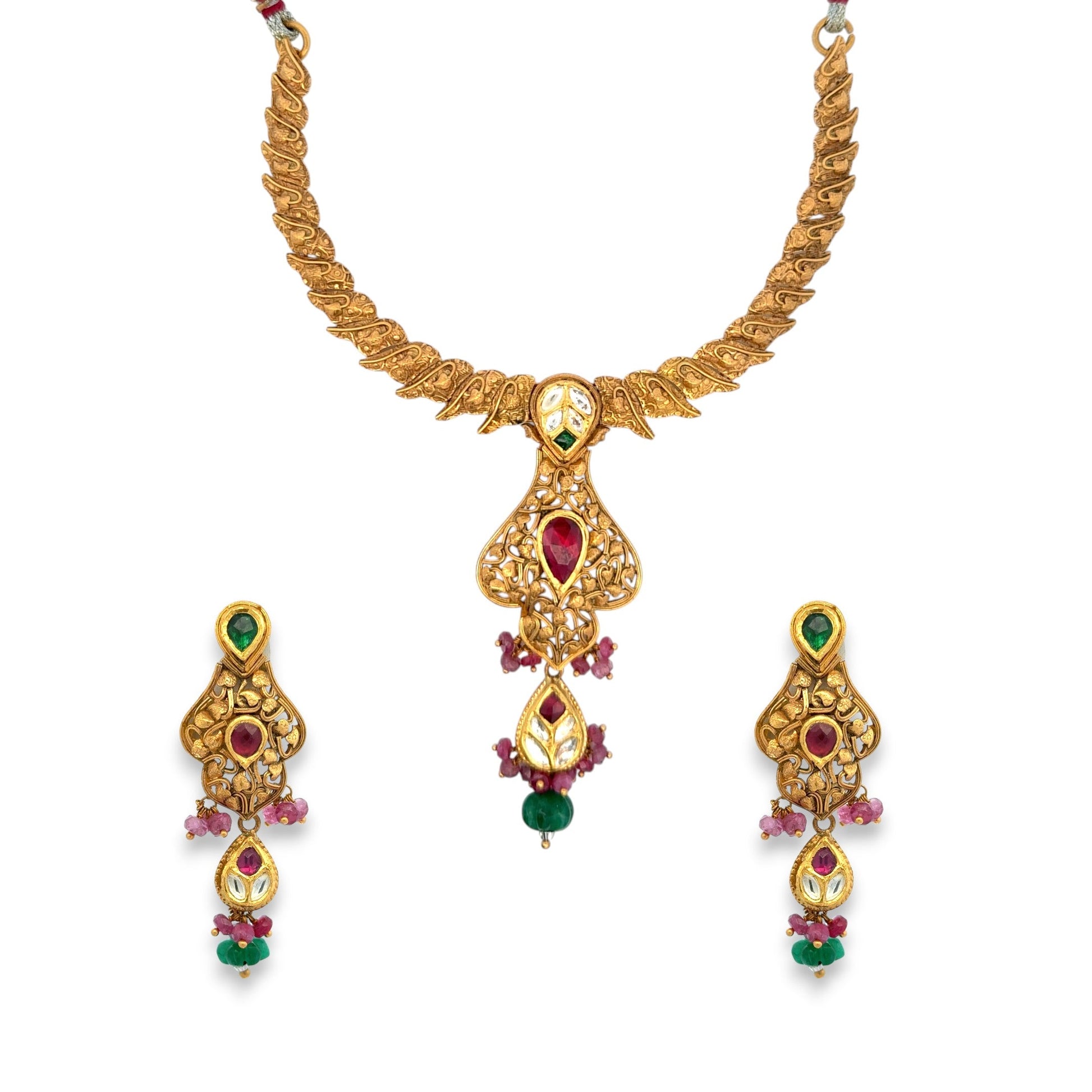 Elegant 22kt gold antique necklace set featuring filigree design with ruby and emerald teardrop stones, accented by Kundan work and gemstone drops. Includes matching earrings, perfect for bridal and festive occasions from Regal Jewels Chicago.