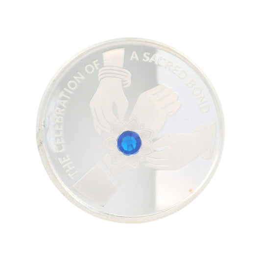 "Regal Jewels RJSB0015 silver coin with Raksha Bandhan theme, featuring engraved hands tying rakhi with a blue gemstone centerpiece, symbolizing the sacred bond of protection – perfect for gifting, festivals, and collectible silver