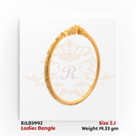 Angled view of a gold ladies bangle featuring an ornate central motif with layered scrollwork, subtle floral engravings, and fine detailing along the band for an elegant traditional touch. Model RJLB3992.