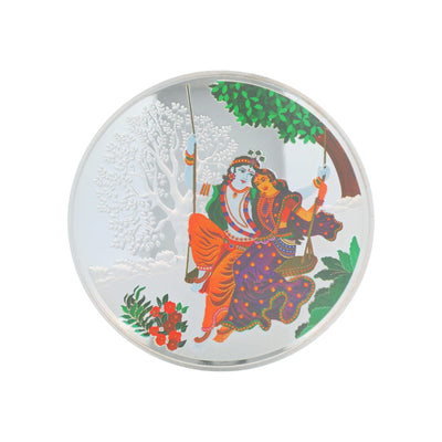 Regal Jewels RJSB0009 silver coin showcasing Radha Krishna seated on a swing beneath a tree with floral detailing – a devotional collectible ideal for puja rituals, festive gifting, and spiritual silver art