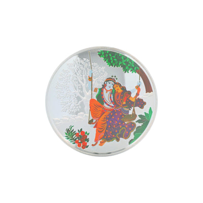 Regal Jewels RJSB0010 silver coin featuring Radha Krishna on a swing under a tree, beautifully detailed with floral and scenic background – perfect for devotional gifting, Hindu puja rituals, and collectible silver art